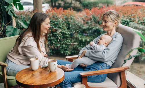 Two women talk about motherhood while nursing a baby while sitting in a cafe.