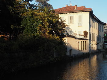 Trees by river and buildings against sky