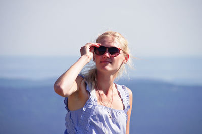 Young woman wearing sunglasses standing against sky