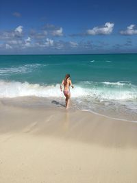 Rear view of woman standing on shore at beach against sky