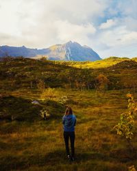 Rear view of woman standing on landscape against cloudy sky