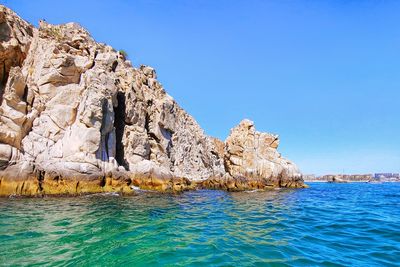 Rock formations in sea against clear blue sky