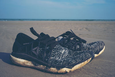 Close-up of shoes on sand at beach against sky