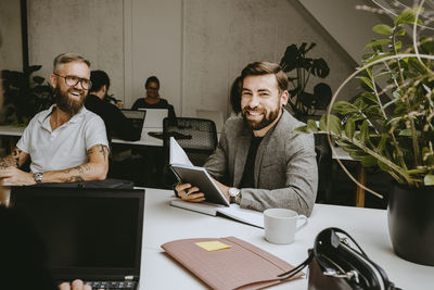 Smiling businessman holding diary while sitting with male colleague in coworking office