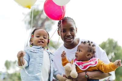 Smiling woman with daughters holding balloons at park