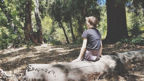 Rear view of woman standing amidst trees in forest