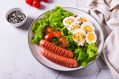 Plate with sausages, egg sandwich, tomatoes and lettuce leaves on the table