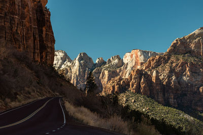 Road amidst rocky mountains against clear blue sky