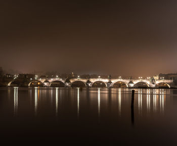 Illuminated city by river against sky at night