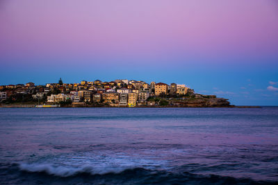 Sea by buildings against sky during sunset