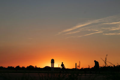 Silhouette trees on field against orange sky