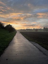 Road amidst field against sky during sunset