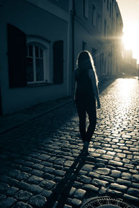 Full length rear view of woman walking on street in city in sunshine