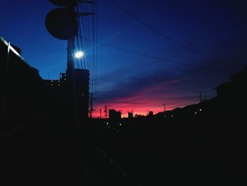 Low angle view of silhouette electricity pylon against sky at night