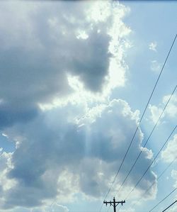 Low angle view of electricity pylon against cloudy sky