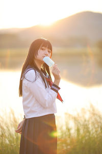 Young woman drinking water while standing outdoors