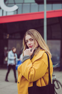 Portrait of beautiful young woman touching chin while standing in city