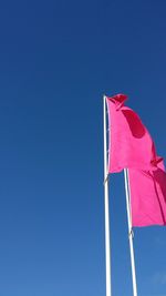 Close-up low angle view of flags against clear blue sky