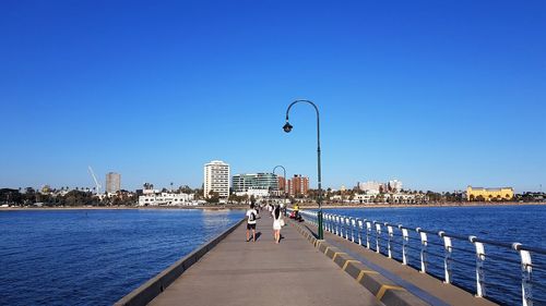 People on sea by cityscape against clear blue sky