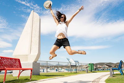 Full length of young woman jumping against sky