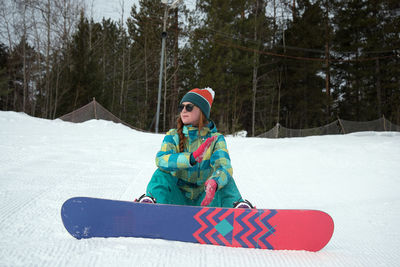 Woman snowboarding on ski slope against trees