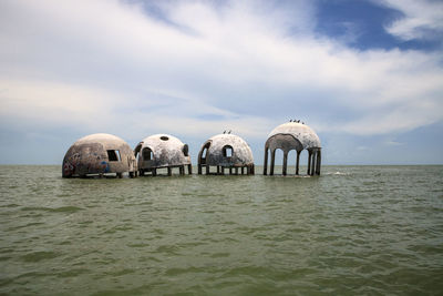 Panoramic view of wooden posts in sea against cloudy sky