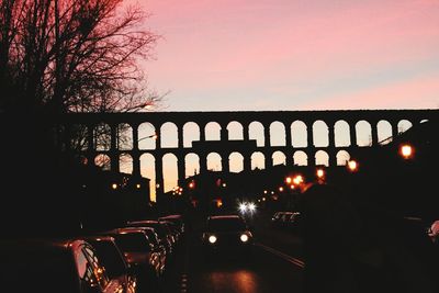 Cars on illuminated road against sky during sunset