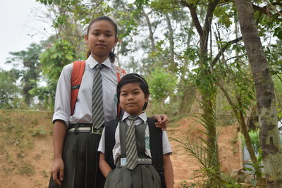 Portrait of sisters in school uniform standing against trees