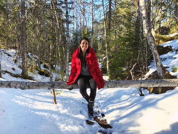 Full length portrait of woman sitting on fallen tree over snow covered land