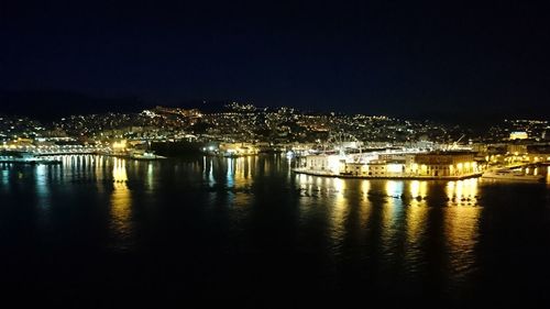 Illuminated buildings by river against sky at night