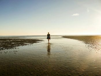 Rear view of woman walking at beach against sky during sunset