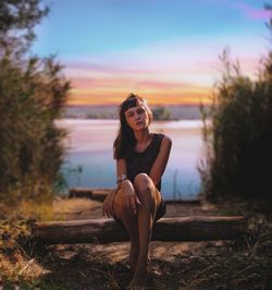 Portrait of woman sitting on land against sky during sunset