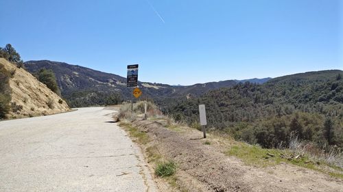 Road sign by mountain against clear blue sky