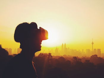 Silhouette man enjoying virtual reality simulator against orange sky