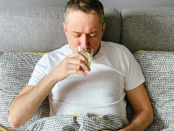 Portrait of young woman eating food on sofa at home