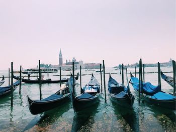 Gondolas moored on canal in city against sky