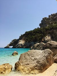 Rock formation by sea against clear blue sky