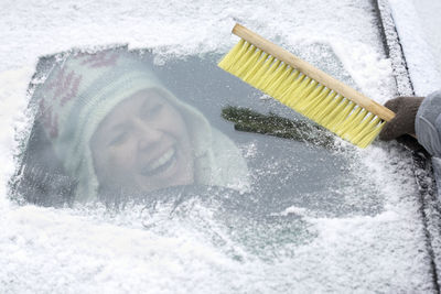 Hand clearing snow from windshield, woman on background