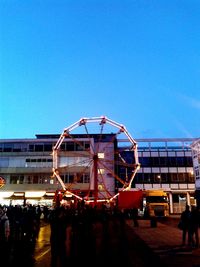 People at amusement park against clear blue sky