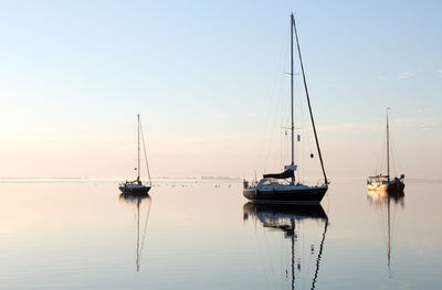 Sailboats moored in sea against sky during sunset