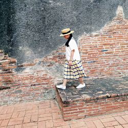 Woman wearing hat standing against wall