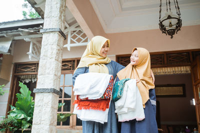 Smiling mother and daughter holding clothes standing outdoors