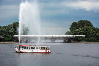 Ferry splashing water in lake against cloudy sky