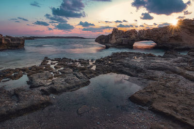 Rocks on beach against sky during sunset