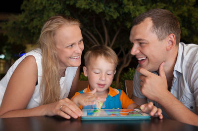 Happy parents with son using digital tablet on table in cafe