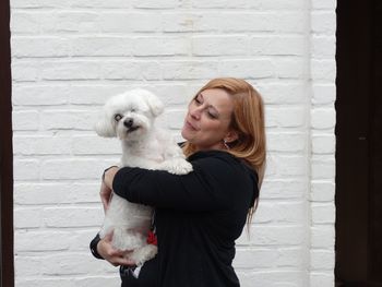 Smiling woman with dog standing against wall