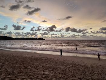 People on beach against sky during sunset