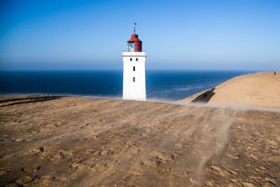 Lighthouse amidst sea and buildings against sky