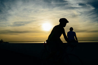 Silhouette man with bicycle against sky during sunset