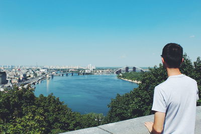 Rear view of man standing against river in city